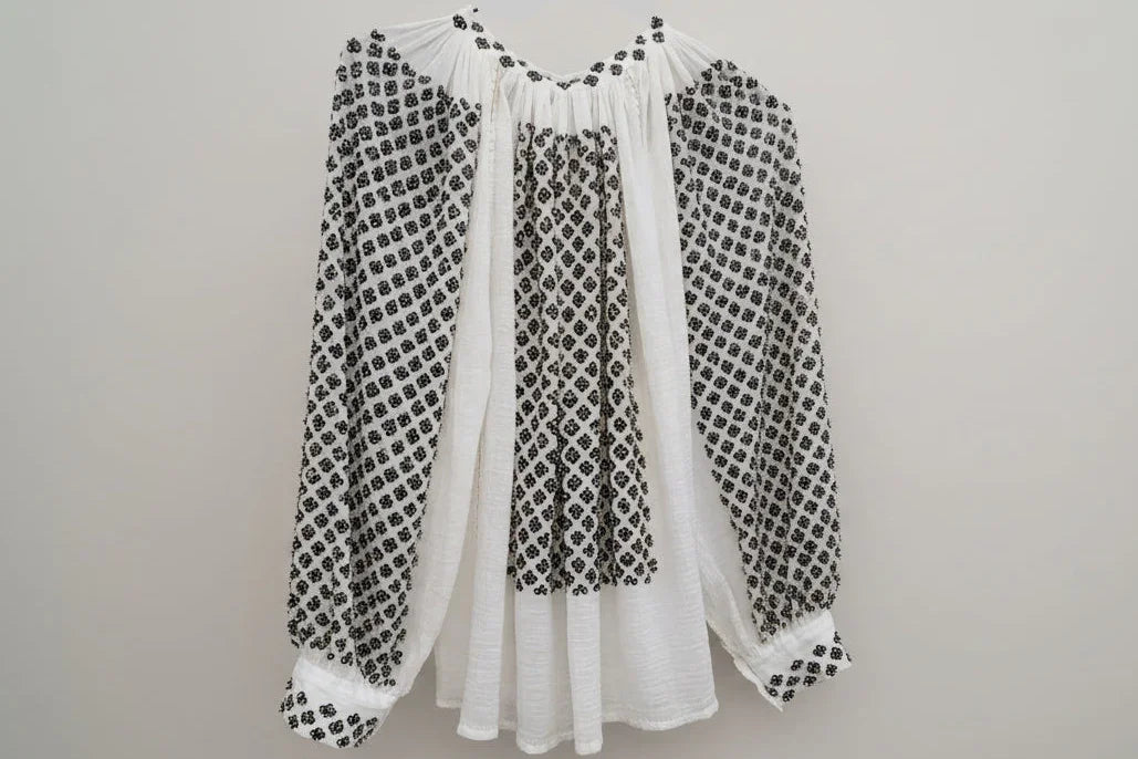 White blouse with black embroidery on a red patterned background