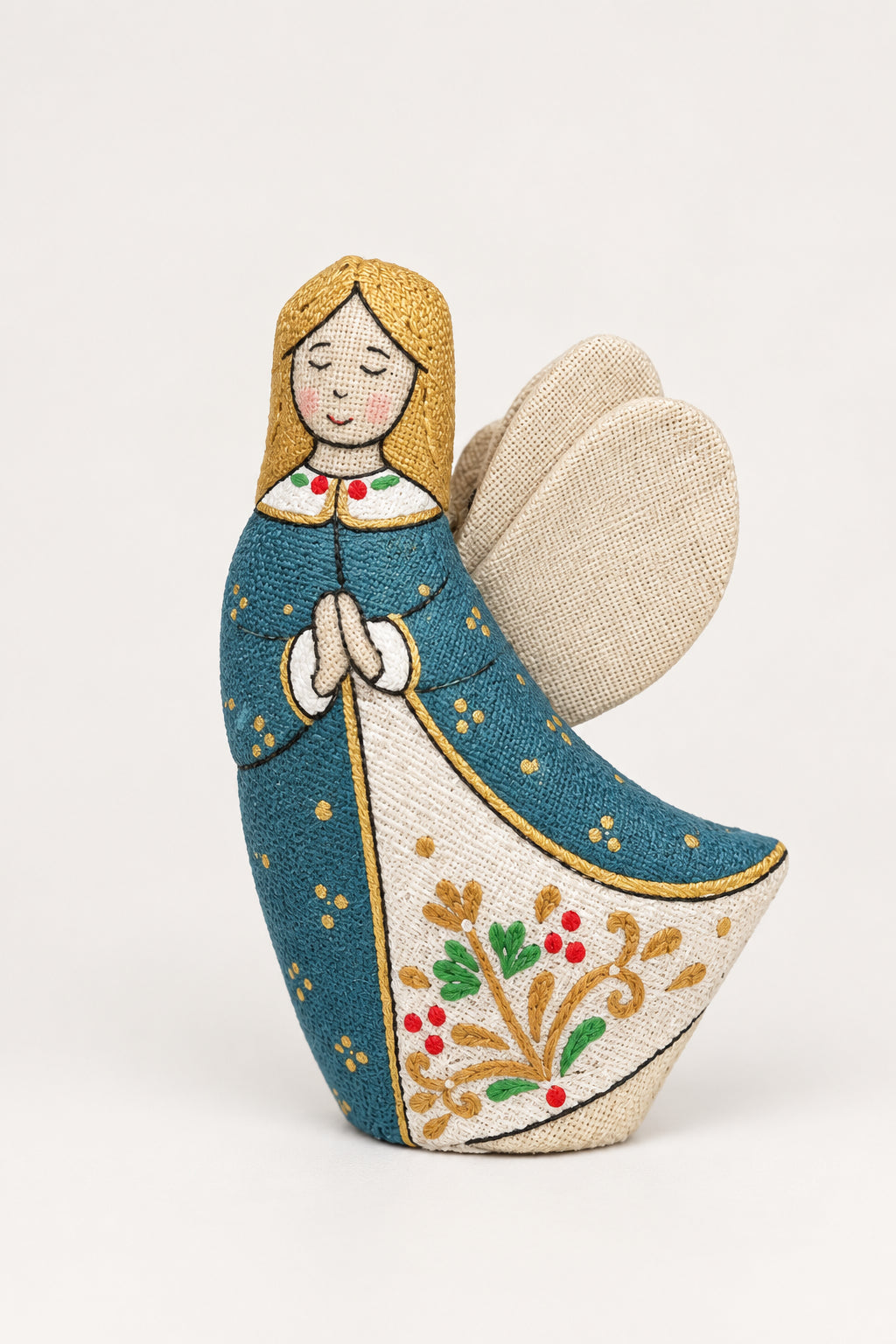 A handmade fabric Christmas angel ornament standing in white snow, with pine branches, silver ornaments, and a blue textured background.