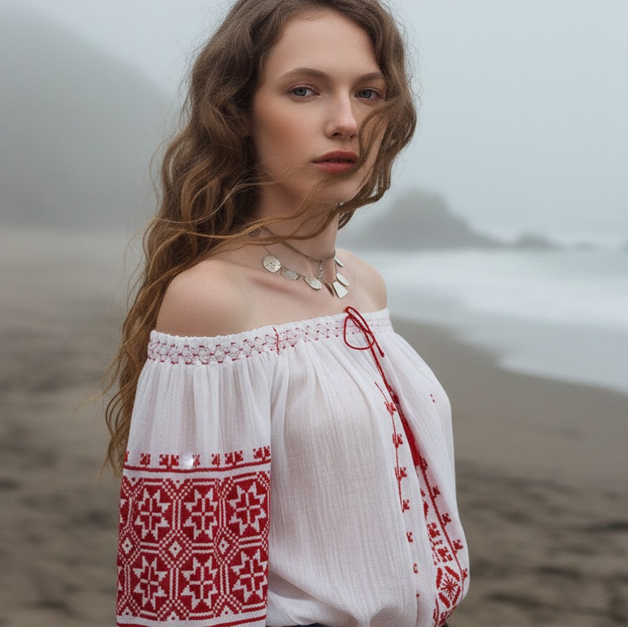 Woman wearing a white off-shoulder blouse with red embroidery on a beach