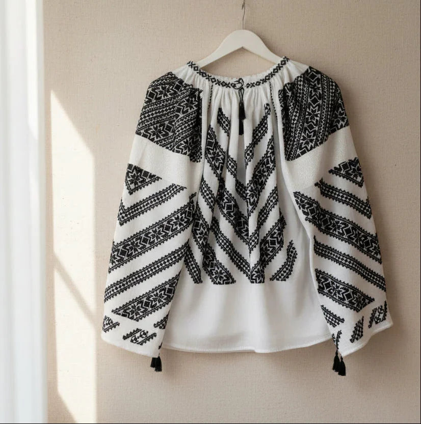 White blouse with black embroidery on a hanger against a white background