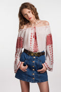 Off-shoulder hand-embroidered Romanian blouse ia with traditional Transylvanian red cross-stitch motifs on white cotton gauze, worn on a misty beach.