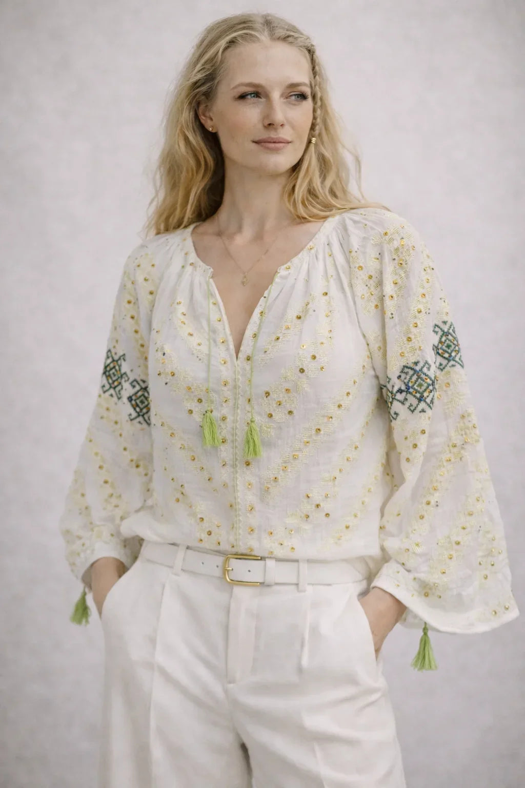 Woman wearing a white blouse with embroidery and tassels on a plain background