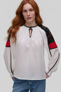 Woman wearing a white blouse with black and red accents on a plain background