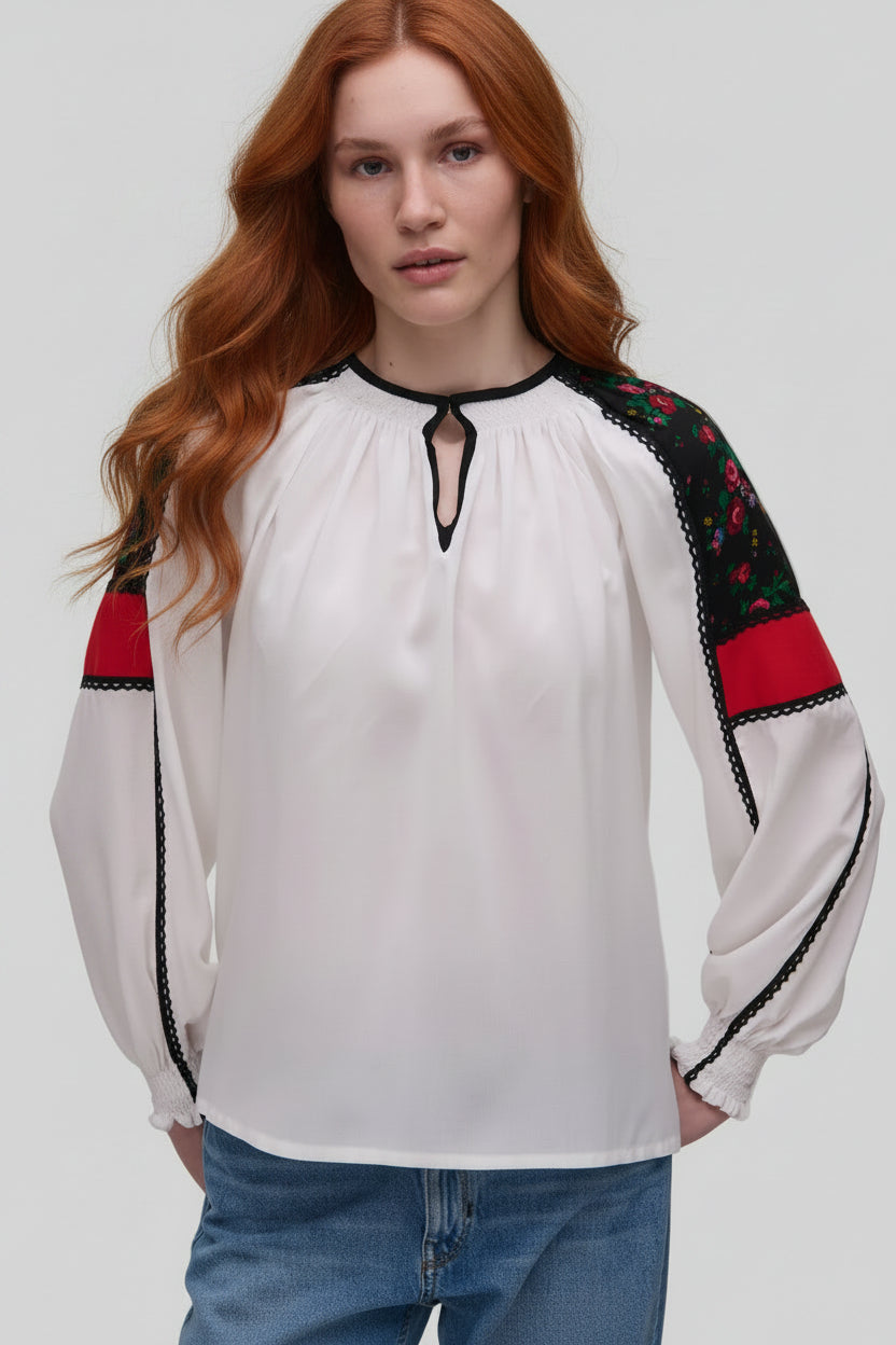 Woman wearing a white blouse with black and red accents on a plain background
