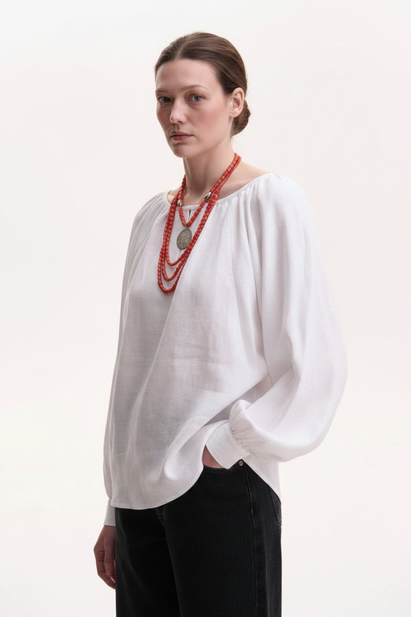 Woman wearing a white blouse and black pants with a red necklace on a white background