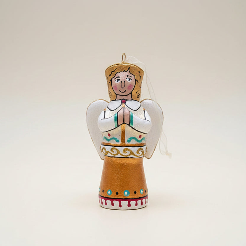 A hand-painted wooden Christmas angel ornament standing on a beige surface against a dark green background. The ornament features a brown body, a white and teal dress, gold hair and trim, and a white veil. Blouse Roumaine Shop Gifs