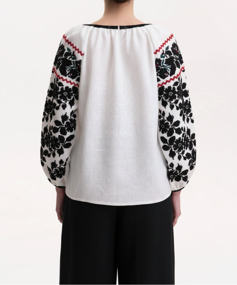 Traditional floral embroidery detail on women’s artisan blouse a white linen blouse with black floral embroidered sleeves and red geometric trim, Blouse Roumaine Shop