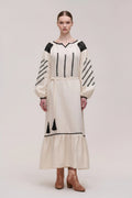 Woman wearing a white dress with black details on a plain background
