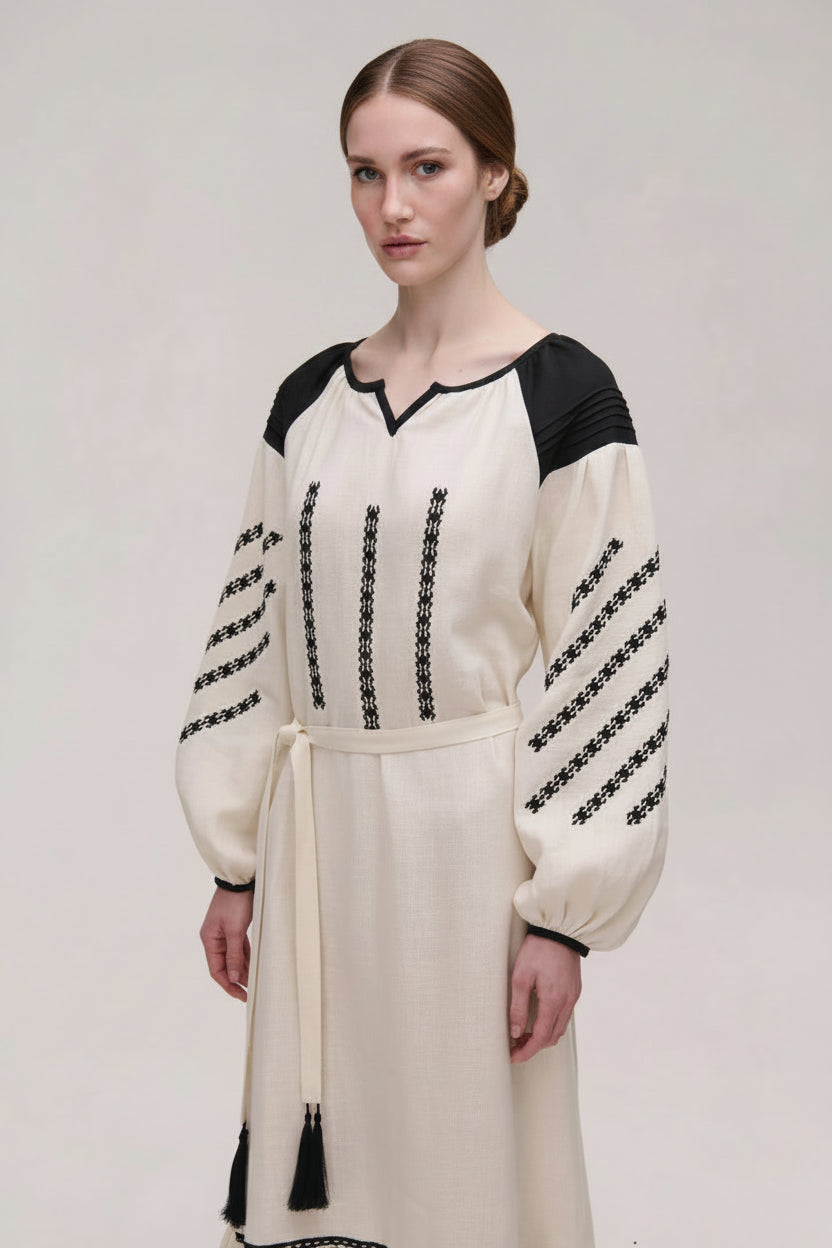 Woman wearing a cream dress with black embroidery on a plain background