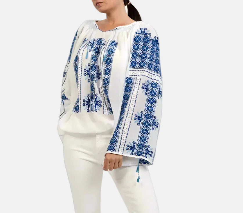 Woman wearing a white blouse with blue embroidery and white pants on a gray background