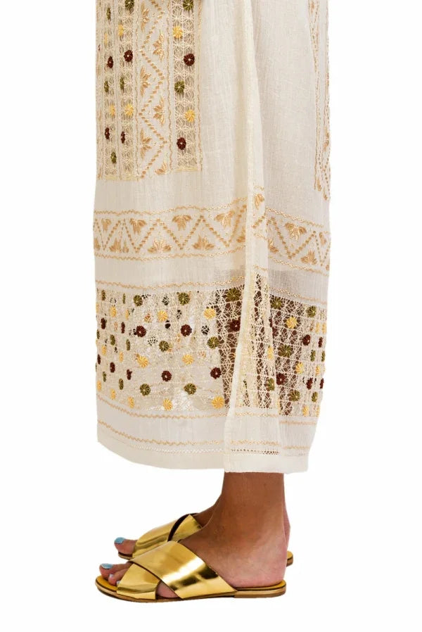 Close-up of a person wearing gold sandals with a white outfit featuring intricate patterns.