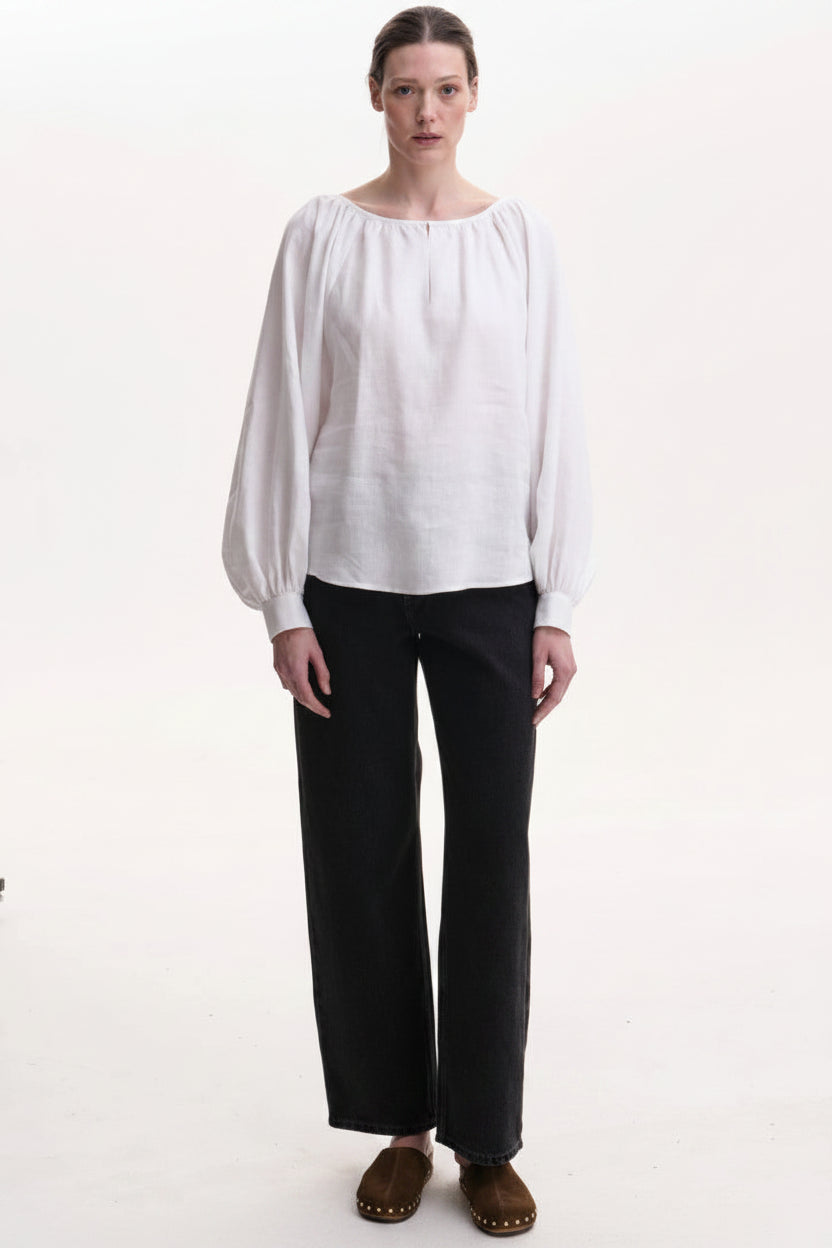 Person wearing a white blouse and black pants with red necklaces on a white background